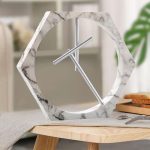 Moderne klok in hexagonale vorm met een frame van wit marmer en metalen wijzers, ideaal voor een elegante en hedendaagse interieurdecoratie.