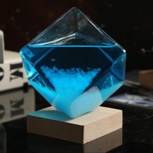 Glazen paneel in de vorm van een kubus met een blauwe vloeistof en een witte poeder op de bodem, geplaatst op een houten sokkel, die een decoratief wetenschappelijk gadget illustreert.