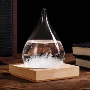 Glazen druppelvormige hanger met een transparante vloeistof, geplaatst op een houten basis, ideaal voor wetenschappelijke decoratie of als origineel accessoire.