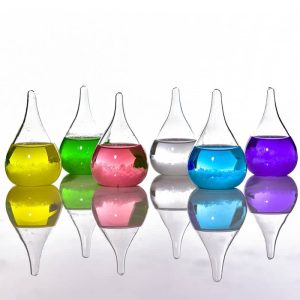 Laboratoriumvazen van glas met gekleurde vloeistoffen in geel, groen, roze, transparant, blauw en paars, in een lijn geplaatst met hun reflectie op een glad oppervlak.