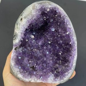 Amethist geode met glanzende paarse kristallen, tentoongesteld op een donkergrijze achtergrond, die de schoonheid en de kristallijne structuur van deze edelsteen benadrukt.