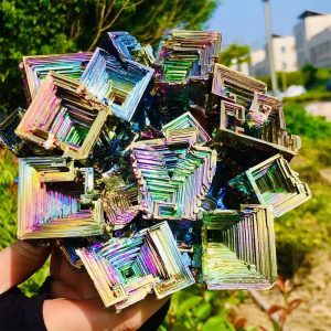 Piramides van holografische, veelkleurige kristallen, glanzend en geometrisch, vastgehouden in de hand met een natuurlijke achtergrond in de open lucht.