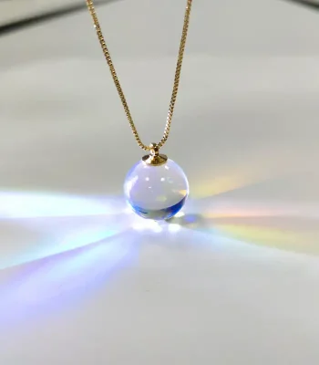 Ketting met een transparante glazen bol als hangertje, die het licht vangt om een lumineus en kleurrijk effect te creëren. Perfect voor liefhebbers van wetenschappelijke decoratie en unieke objecten.