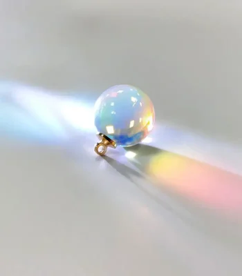 Kleine kristallen bol met regenboogreflectie die gekleurd licht op een witte ondergrond projecteert, wat een boeiend en mysterieus visueel effect creëert.