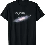 Sterrenstelsel T-shirt met tekst "You're Here" in het wit op een zwarte achtergrond, dat een spiraalvormig sterrenstelsel met een humoristische en kosmische boodschap weergeeft.